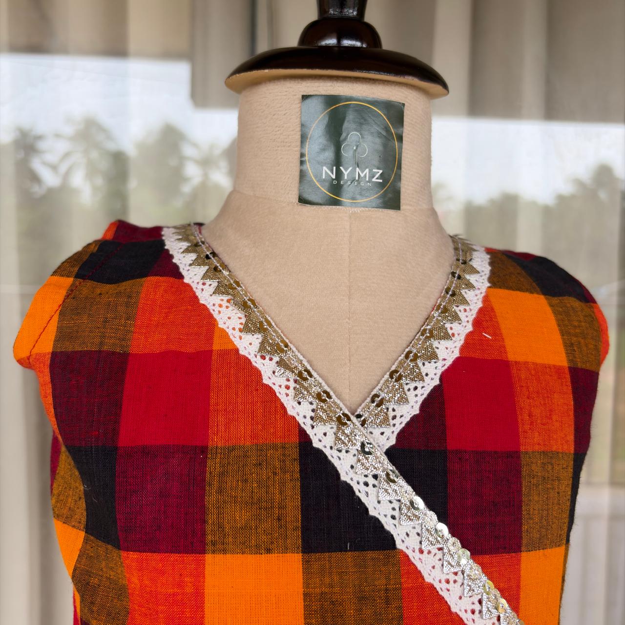 A cropped plaid top in orange, red, black, and brown, featuring a white lace V-neck trim with gold sequins, displayed on a beige mannequin torso. The mannequin has a visible NYMZ brand label.