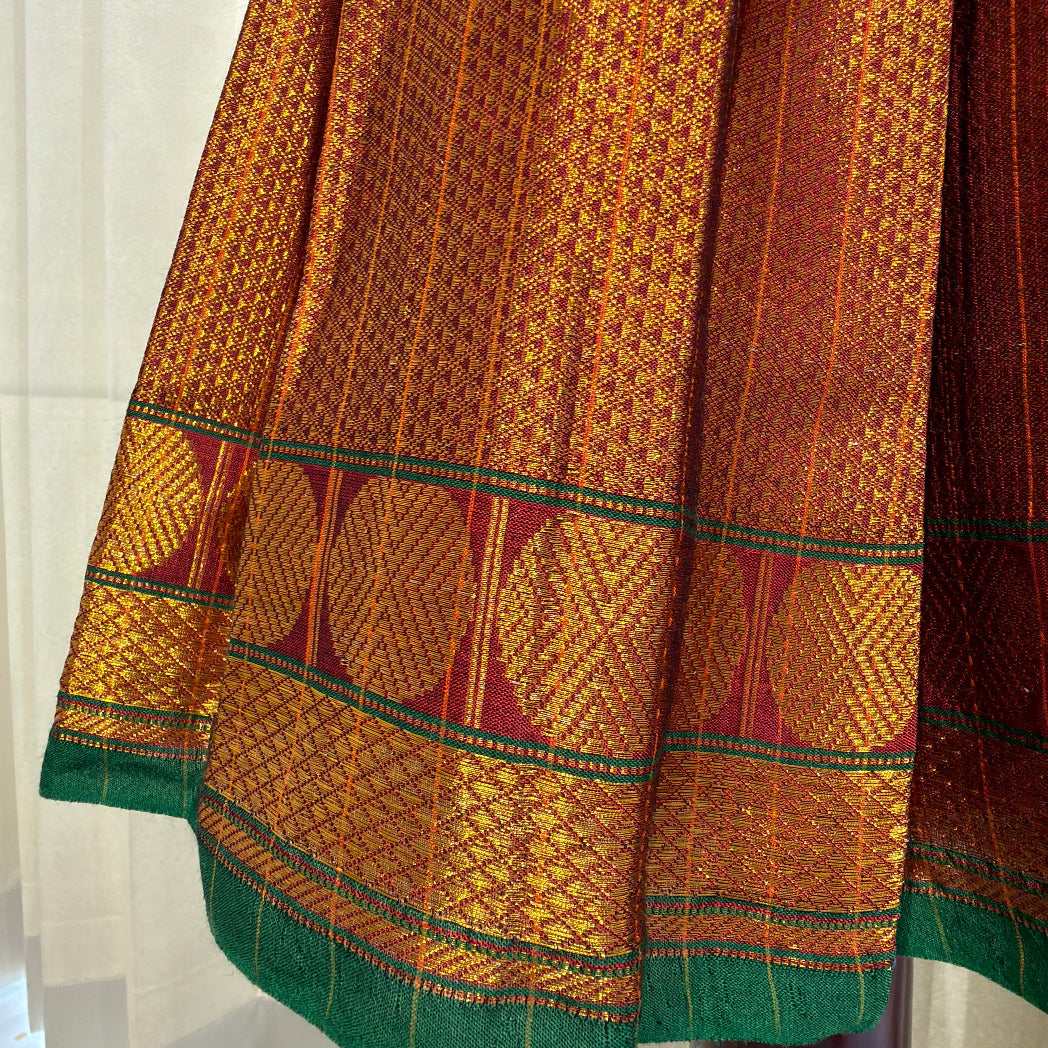 A close-up of a traditional Indian narayanpet lehanga ,showcasing its rich golden-yellow and brown woven body with a green border and red accents.