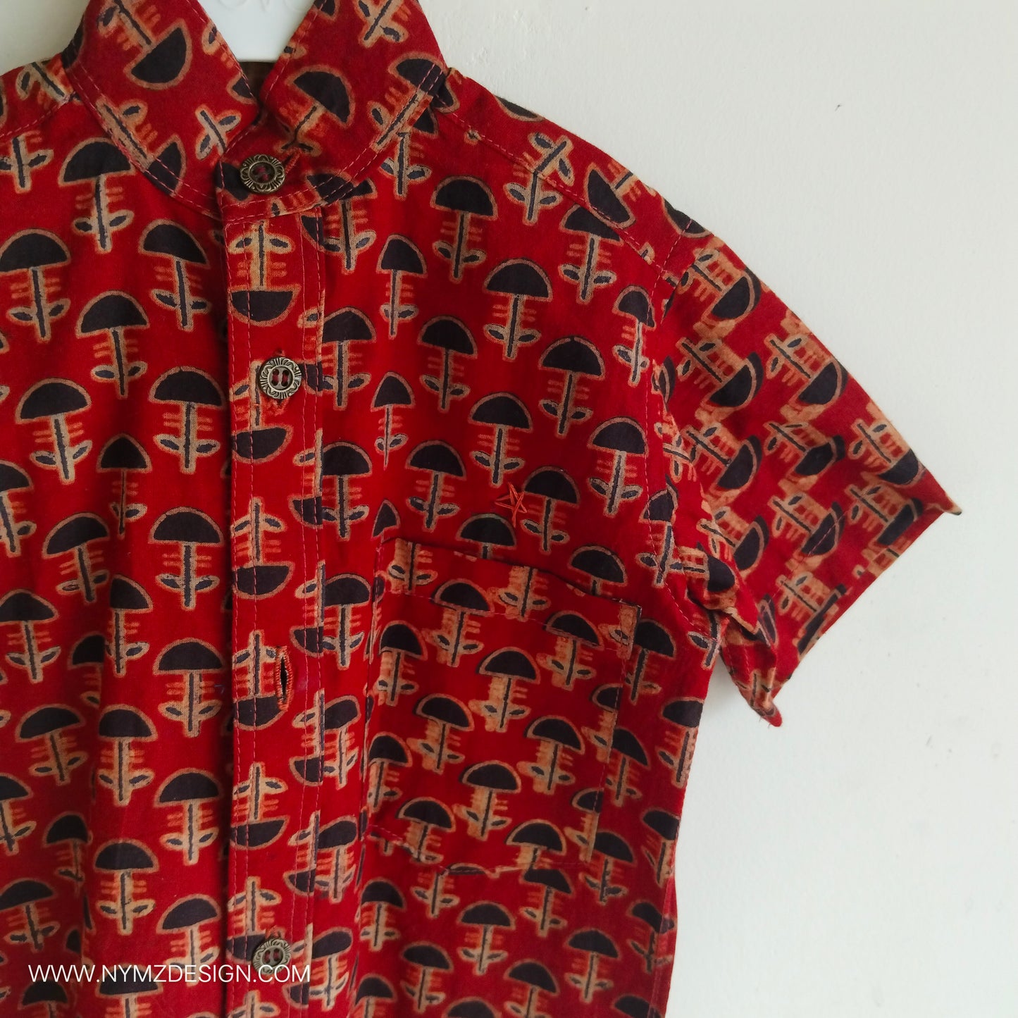 Close-up of star hand embroidery near pocket on Ajrakh brick red cotton kids shirt – handcrafted Indian handblock print design.metal buttons