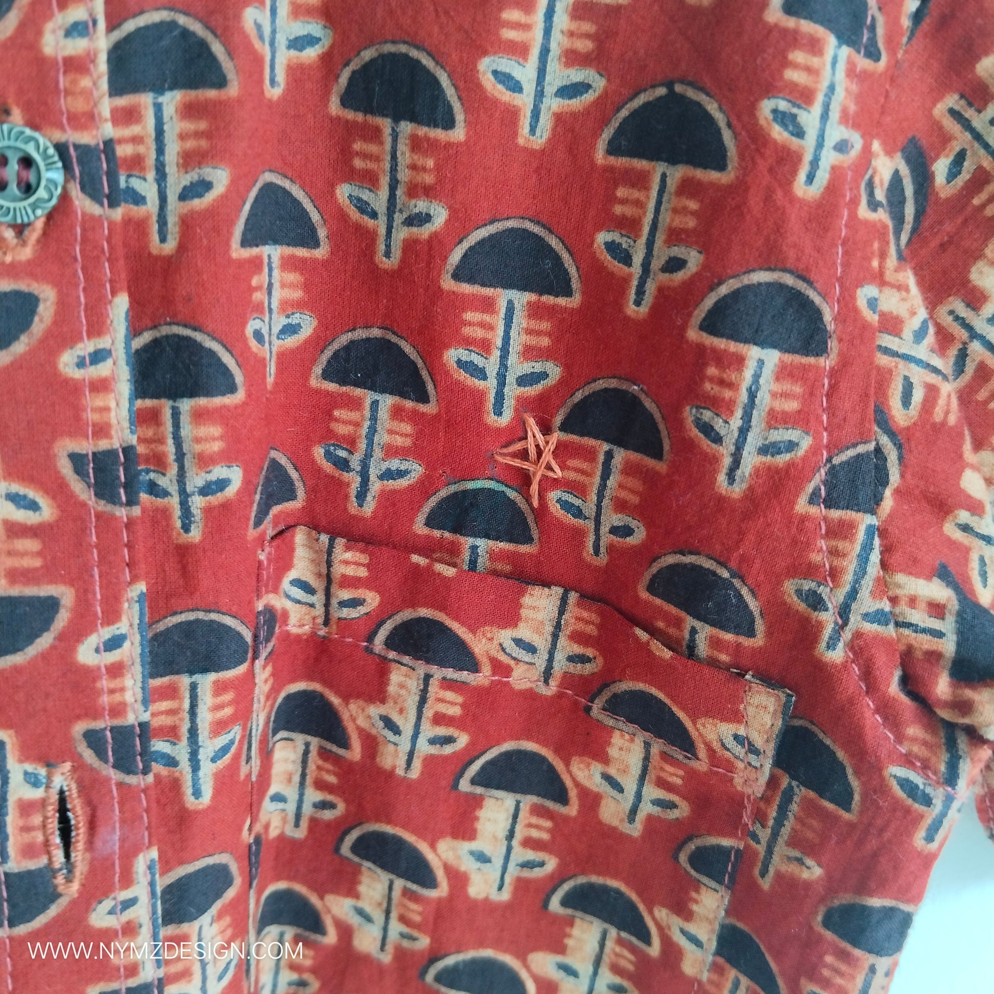 Close-up of star hand embroidery near pocket on Ajrakh brick red cotton kids shirt – handcrafted Indian handblock print design